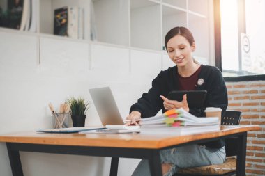 Ofisteki iş raporunu incelemek için tablet ve laptop kullanan kadın iş kadını