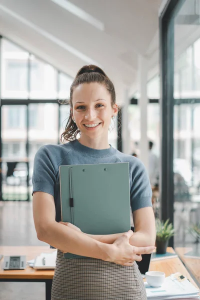 Successful businesswoman standing in creative office and looking on camera. Woman entrepreneur in a coworking space smiling.