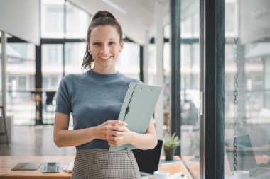Başarılı iş kadını yaratıcı ofiste dikilip kameraya bakıyor. İş yerinde çalışan kadın girişimci gülümsüyor..