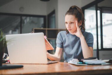 Ciddi meşgul genç iş kadını yöneticisi dizüstü bilgisayara bakıyor finansal dijital piyasa risklerini düşünüyor, yeni kurumsal strateji fikrini düşünüyor, webinar izliyor..