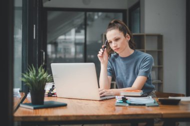 Genç iş kadını, portatif dizüstü bilgisayarın önünde oturup müşteriden gelen e-postayı okurken bir şey düşünüyor.