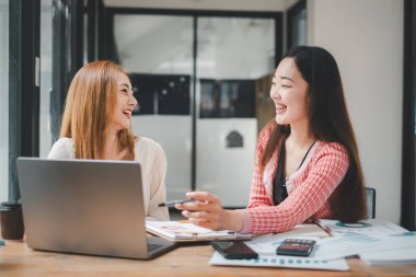 Ofiste dizüstü bilgisayar kullanan neşeli iş adamları. Modern bir çalışma alanında birlikte çalışırken gülümseyen genç girişimciler. Masada birlikte oturan iki genç iş adamı..
