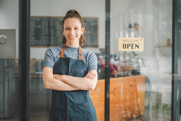 Portrait of happy waitress standing at restaurant entrance with open sign, Portrait of young business woman attend new customers in her coffee shop.