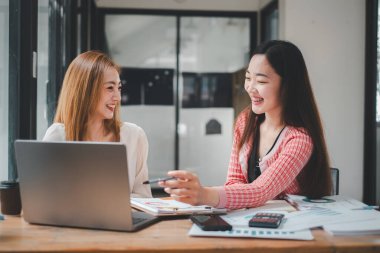 Meşgul ve hevesli iş kadınları modern ofis ortamında dizüstü bilgisayar kullanarak bir proje üzerinde birlikte çalışıyorlar.