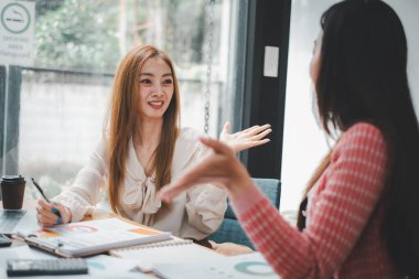 İki meşgul iş kadını, takım çalışması ve planlama üzerine yoğunlaşarak, ortak bir iş toplantısı sırasında sohbet ediyorlar.