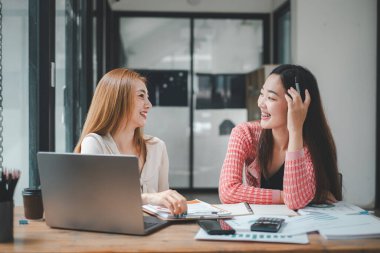 İki neşeli bayan meslektaşımız parlak bir ofis ortamında iş fikirlerini tartışırken neşeli bir anı paylaşıyorlar.