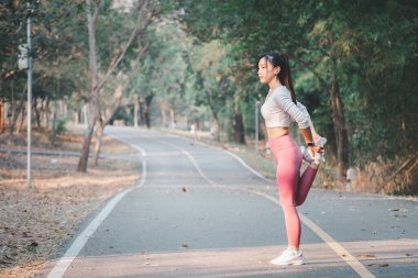 Koşu konsepti, genç bir bayan sporcu sakin bir park yolunda koşmadan önce bacak kaslarını esnetir.