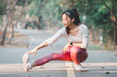 Koşu konsepti, hareketli bir kadın güneş ışığıyla aydınlanan bir park yolunda dizlerini esnetiyor, fiziksel kondisyonuna odaklanıyor.