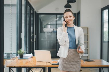 İş kadını konsepti, gülümseyen genç iş kadını masadaki bilgisayarla telefon görüşmesi yapıyor.