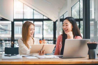 İş dünyası analiz konsepti, gülümseyen bayan meslektaşlar, parlak bir ofis alanında dizüstü bilgisayar ve defterle birlikte çalışıyorlar.