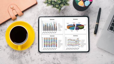 Modern bir çalışma alanının en üst görüntüsü, bir tablette sergilenen mali raporun yanı sıra bir dizüstü bilgisayar ve bir fincan kahve.