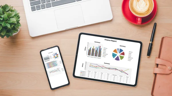 Modern bir çalışma alanının en üst görüntüsü, bir tablet ve akıllı telefonda sergilenen mali raporla birlikte, bir dizüstü bilgisayar ve bir fincan kahvenin yanı sıra
