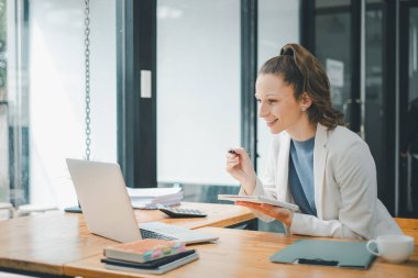 İş analizi konsepti, ofis masasındaki odaklanmış iş kadını bir dizüstü bilgisayarla meşgul ve bir deftere notlar alıyor..