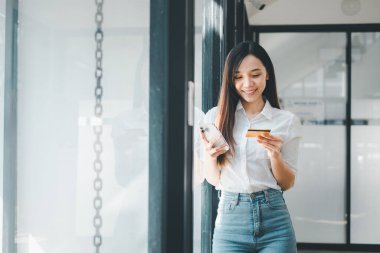 Buiness Teknoloji konsepti, gündelik giysiler içinde gülümseyen genç bir kadın akıllı telefonu ve kredi kartıyla online ödeme yapıyor..