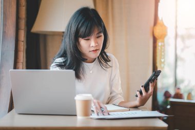 Ticari serbest meslek kavramı, genç Asyalı profesyonel bir kadın çalışma alanındaki akıllı telefonundaki verileri incelemeye dalmıştır.