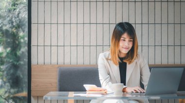 Serbest meslek sahibi bir kadın, modern bir kafede dizüstü bilgisayarıyla çalışır. Masasında kahve ve akıllı telefon bulunur.