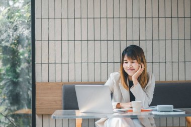 Serbest meslek sahibi bir kadın, modern bir kafede dizüstü bilgisayarıyla çalışır. Masasında kahve ve akıllı telefon bulunur.