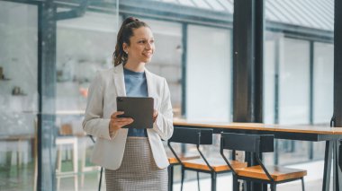 İş analitiği konsepti, kendine güvenen kadın profesyonel gülümseyen ve dijital tableti doğal ışık alan çağdaş bir ofis alanında tutan.