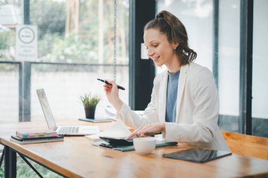 İş analizi konsepti, odaklanmış bir iş kadını, ahşap ofis masasında dizüstü bilgisayar ve not defteriyle programını planlıyor..