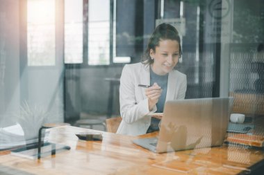 İş analizi konsepti, iyi aydınlatılmış bir ofis ortamındaki ahşap bir masada dizüstü bilgisayarıyla çalışan gülümseyen profesyonel kadın..