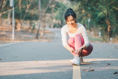 Spor salonu ve koşu konsepti aktif genç kadın spor yaparken ayakkabı bağcıklarını güneş ışığında bağlamak için duruyor..