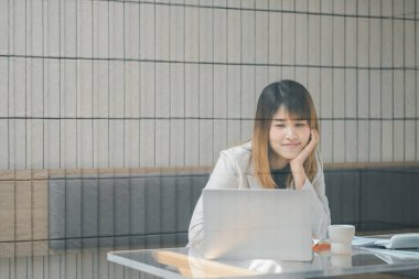 Serbest meslek sahibi bir kadın, modern bir kafede dizüstü bilgisayarıyla çalışır. Masasında kahve ve akıllı telefon bulunur..