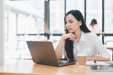 İş ve teknoloji konsepti, kahve masasında dizüstü bilgisayarı üzerinde dikkatle çalışan düşünceli profesyonel bir kadın, yanında kahve fincanı ve not defteri..