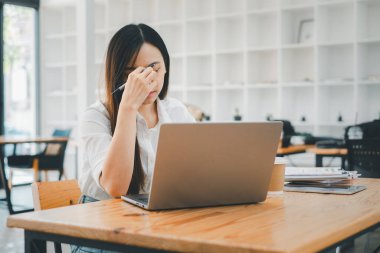 İş ve teknoloji kavramı, stresli genç bir kadın profesyonel, modern çalışma ortamında dizüstü bilgisayar ekranına bakarken alnını ovalıyor..