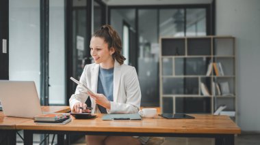 İş analitiği konsepti, neşeli iş kadını günümüzün ofisinde dizüstü bilgisayarla tahta bir masada otururken programını bir defterle düzenliyor.
