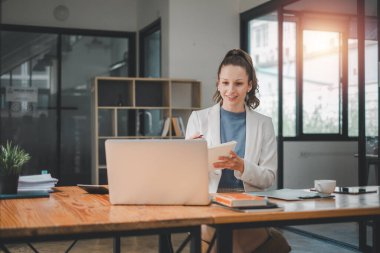 İş analitiği konsepti, dizüstü bilgisayar kullanan ve elinde parlak, modern bir ofis ortamında defter tutan gülümseyen profesyonel bir kadın.