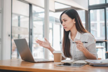 İş analizi konsepti, profesyonel Asyalı iş kadını kahve ve notlarla dolu, parlak bir kafe ortamında dizüstü bilgisayar üzerinde çalışıyor.