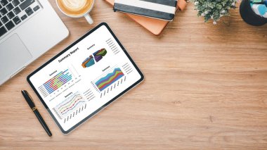 Dijital tabletin yer aldığı organize bir masa grafikler ve analizlerle birlikte bir iş özeti raporunu bir fincan taze kahvenin yanında gösteriyor.