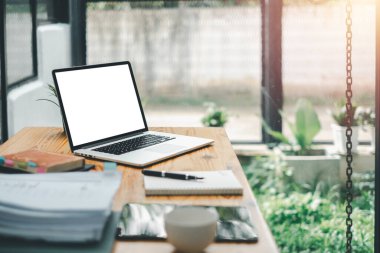 Boş ekranlı bir dizüstü bilgisayar, defterler ve parlak bir ofisteki ahşap bir masanın üzerine yerleştirilmiş bir bitki içeren organize bir çalışma..