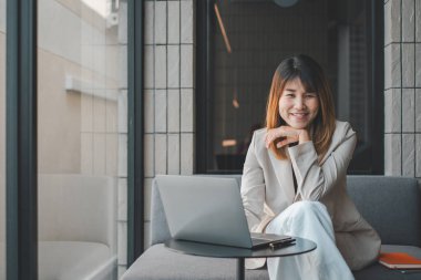 Gülümseyen bir iş kadını, şık bir ofis ortamının çağdaş ortamında dizüstü bilgisayarla çalışmaktan zevk alır..
