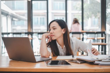 Düşüncelere dalmış genç bir iş kadını iş stratejisini dizüstü bilgisayarı ve bir kafe masasında notlarla planlar..