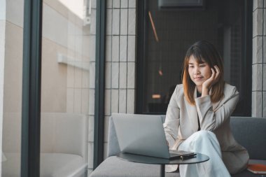 Kendini işine adamış ve işine odaklanmış bir iş kadını, sakin bir kentsel çevre ile çevrili bir kafede dizüstü bilgisayarla uğraşıyor..