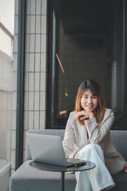 Gülümseyen bir iş kadını, şık bir ofis ortamının çağdaş ortamında dizüstü bilgisayarla çalışmaktan zevk alır..