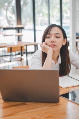 İş problemleri çözme konsepti, düşünceli bir kadın çenesini elinde tutarak oturur, laptopundan kafasını çevirir, parlak bir ofis odasında derin düşüncelere dalmıştır..