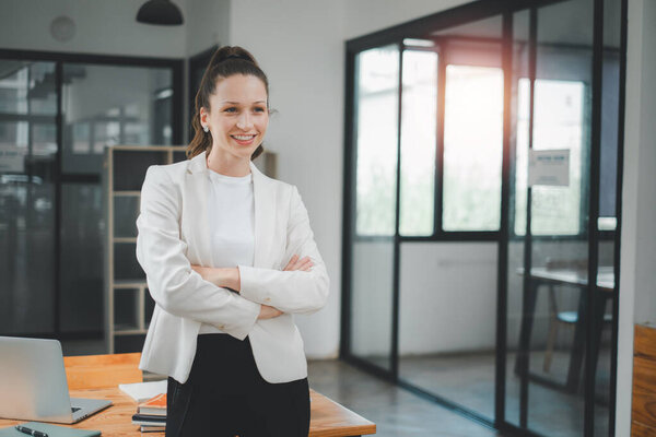 Business management concept, A confident, smiling businesswoman stands with crossed arms in a bright, contemporary office setting, exuding professionalism.