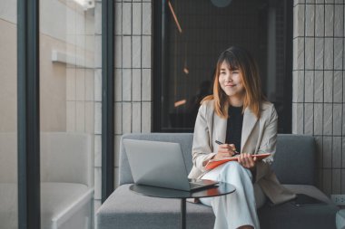 Bir iş kadını yaratıcı bir beyin fırtınası seansına katılır, düşüncelerini not defterine yazar, düşünceli bir gülümsemeyle, iyi aydınlatılmış modern ofis alanında..