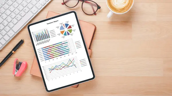 An organized workspace featuring a tablet with detailed analytical charts, next to office essentials and a cup of latte, illustrates a data-driven approach to business decision making.