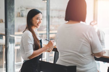 Gülümseyen bayan garson sipariş alır restoran ziyaretçileri ile konuşur, arkadaş canlısı profesyonel kadın garson önlüğü giyer yemek menüsü seçer, iyi müşteri hizmetleri sunar.