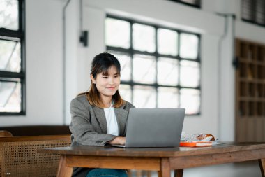 Modern bir ofiste dizüstü bilgisayarla çalışırken gülümseyen genç profesyonel bir kadın..