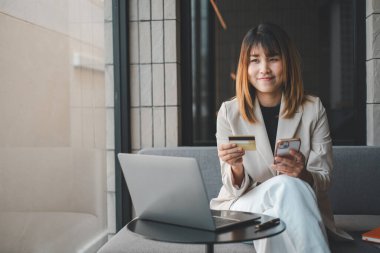 Mobil Alışveriş. Çevrimiçi akıllı telefon alışverişi yapan neşeli bir kadın elinde kredi kartıyla evdeki kanepede oturarak ödeme yapıyor. İnternet bankacılık uygulaması ve e-ticaret.