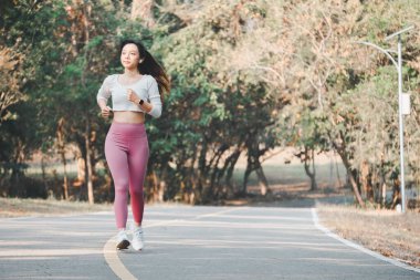 Pembe tayt ve beyaz spor ayakkabı giyen neşeli bir koşucu yeşil bir yolda koşarken mutluluk ve sağlık yayar..