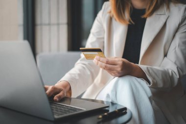 Modern bir ortamda profesyonel bir kadın, çağdaş e-ticaret ve iş dünyasının sembolü olan bir kredi kartı ve dizüstü bilgisayar kullanarak güvenli bir şekilde online alım yapıyor..
