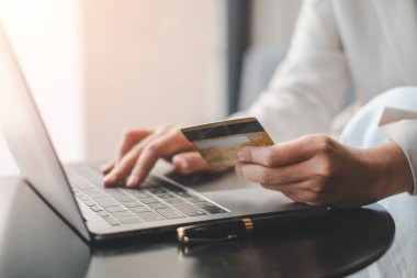 Çevrimiçi ödeme yapan ellerin yakın çekimi, bir elinde bir kredi kartı, diğer elinde ise bir dizüstü bilgisayarla, güvenli dijital işlemleri gösteriyor..