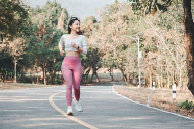 Pembe tayt ve beyaz spor ayakkabı giyen neşeli bir koşucu yeşil bir yolda koşarken mutluluk ve sağlık yayar..