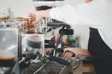 Siyah önlüklü yetenekli bir barista bir espresso makinesini ustalıkla çalıştırıyor ve mükemmel bir fincan kahve yapmaya odaklanıyor..