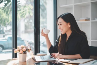 Ofiste dizüstü bilgisayar kullanan güzel bir iş kadını kahve içerken rahatlatıcı bir konsept kullanıyor..